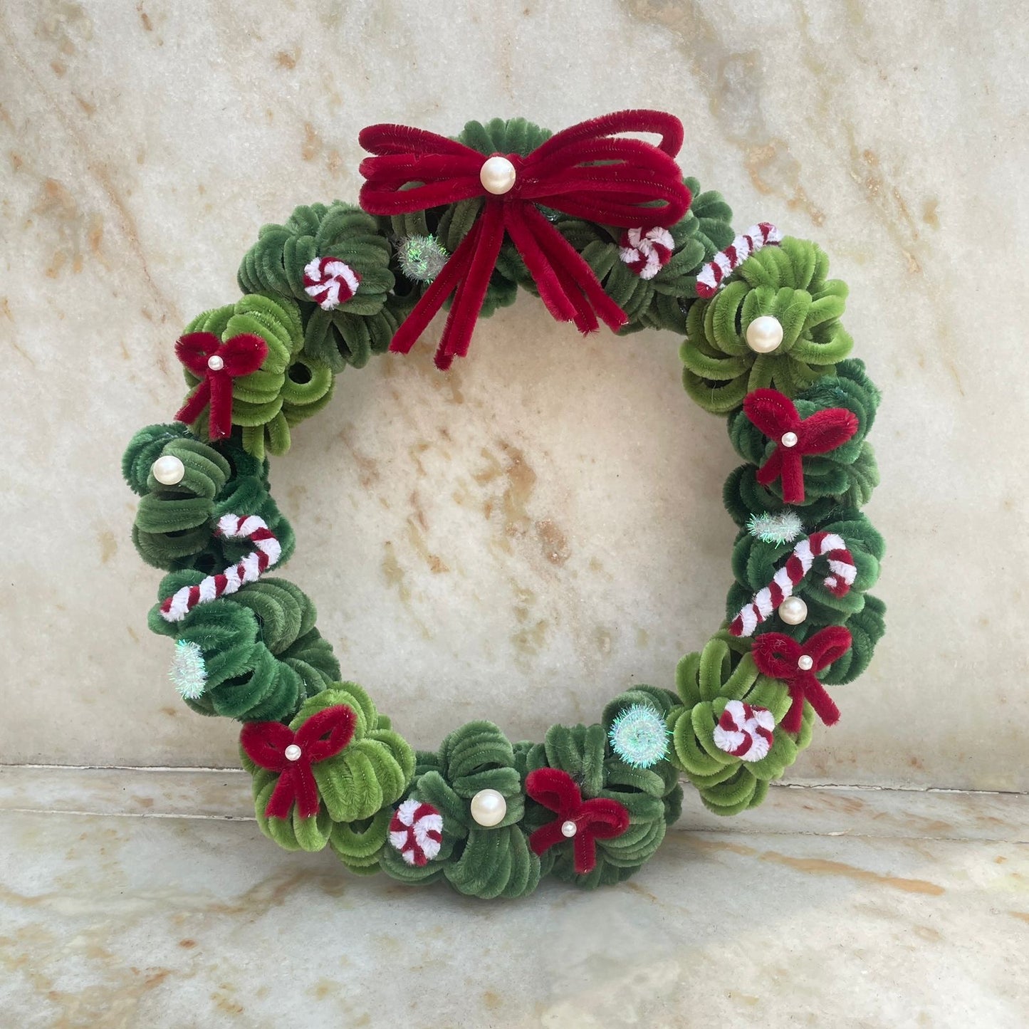 Decorative Christmas wreath with green leaves, red bows, and candy cane details on a marble surface made using high quality pipe cleaners