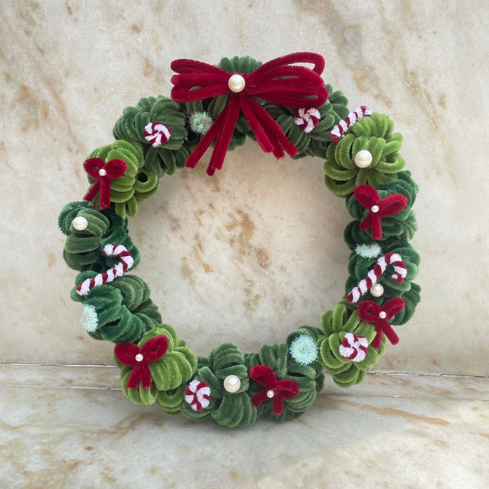 Decorative Christmas wreath with green leaves, red bows, and candy cane details on a marble surface made using high quality pipe cleaners