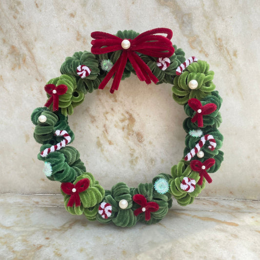 Decorative Christmas wreath with green leaves, red bows, and candy cane details on a marble surface made using high quality pipe cleaners