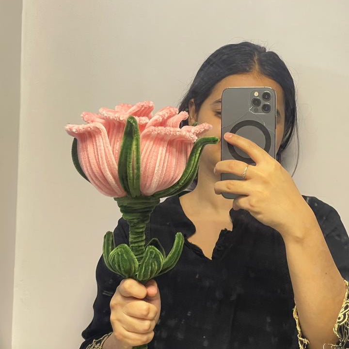 Person holding a large peach pink rose made with pipe cleaners in front of a mirror